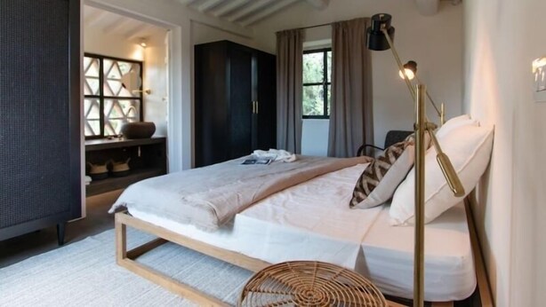 A bedroom with a bed, bedside lamp, and a view of the outdoors.