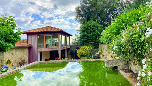 A two-story house with a red-tiled roof, a glass conservatory, and a small pond in the backyard.