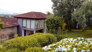 A house with a red-tiled roof and a balcony overlooking a garden with hydrangeas and various shrubs.