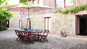 A stone building with a courtyard table set for four, surrounded by stone walls and red shutters.