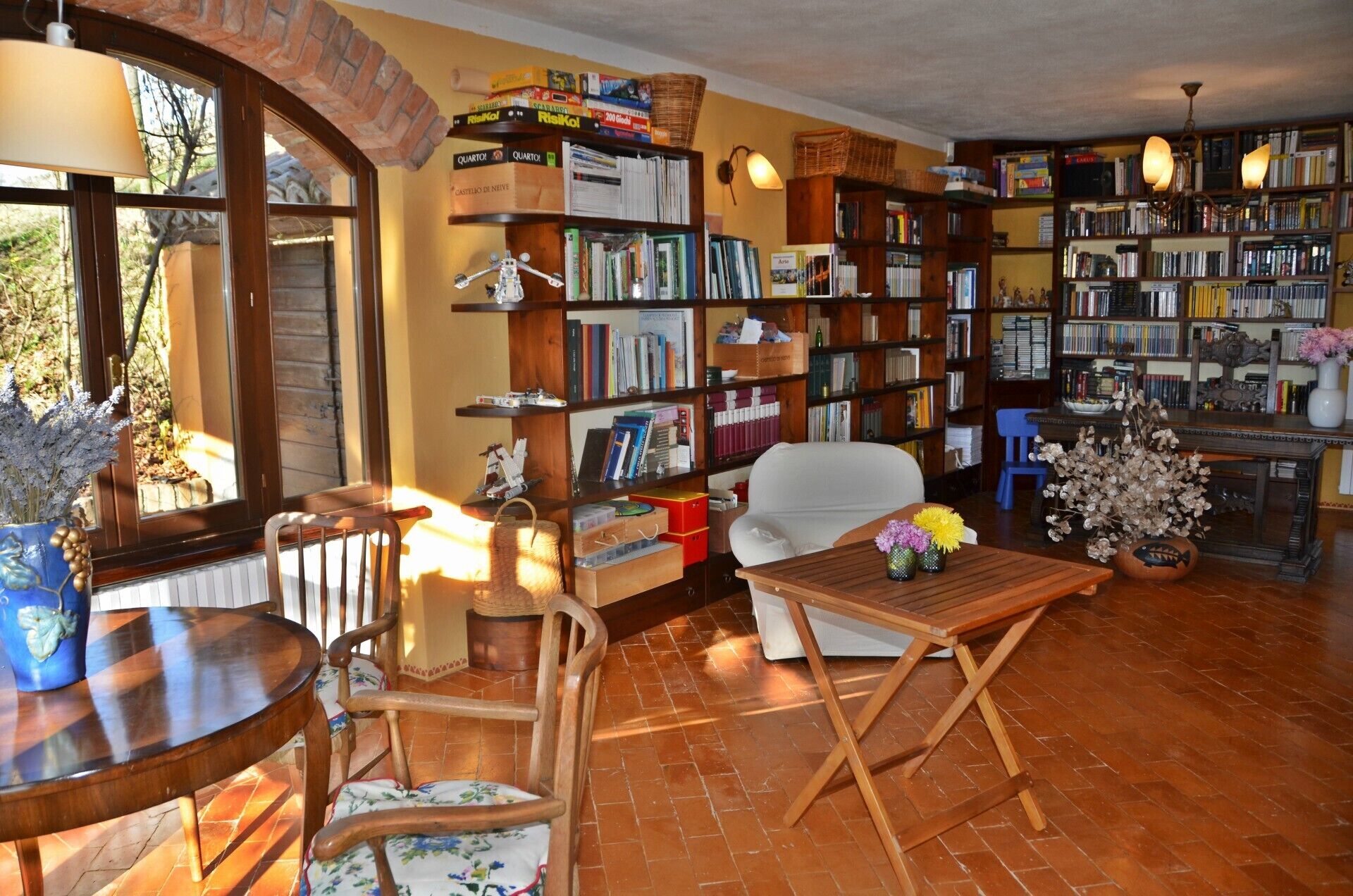 Un salon chaleureux avec une cheminée, une bibliothèque remplie de livres, un fauteuil confortable et une table ornée d’un vase de fleurs.