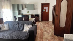 Uma sala de estar com sofá, um espaço de jantar com mesa e cadeiras, uma cozinha com armários e uma porta de madeira.