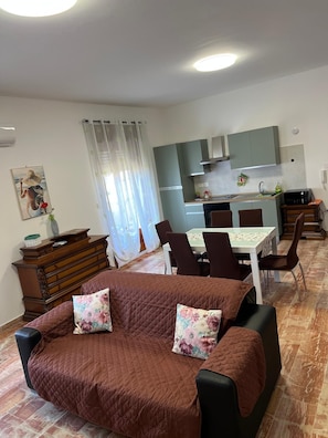 A living room with a sofa and chairs, a dining table, and a kitchen area with cabinets and a microwave.