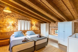 Una habitación rústica con vigas de madera, una pared de piedra, dos camas, un armario y una ventana.