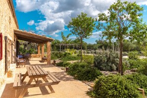 Un patio al aire libre con mesas y sillas de madera, rodeado de plantas y árboles.