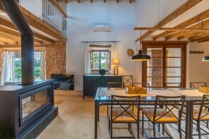 Un interior rústico con una pared de piedra, una chimenea, una zona de comedor con mesa y sillas, y un techo de madera.