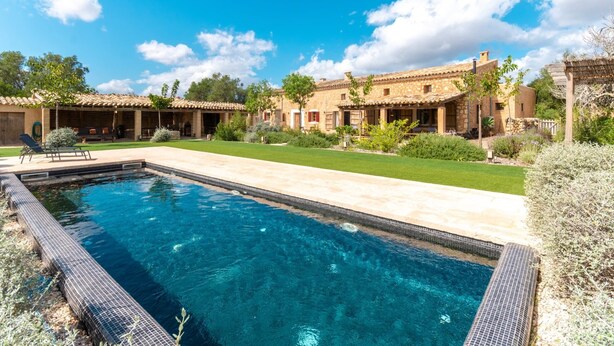 A swimming pool with a tiled deck, surrounded by a well-maintained lawn and a stone building with a tiled roof.
