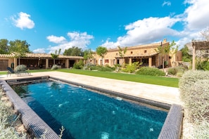 A swimming pool with a tiled deck, surrounded by a well-maintained lawn and a stone building with a tiled roof. - CA'N CORTANA - Stylish house in the heart of the island. (Inca)