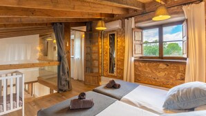A rustic room with wooden beams, a balcony, and a large window with a view.