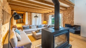 A cozy living room with a stone wall, wooden beams, a sofa, a fireplace, and a TV mounted on the wall.
