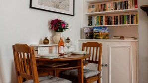 Zona pranzo con tavolo in legno apparecchiato per due, un vaso con fiori e una libreria piena di libri.