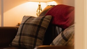 Un soggiorno accogliente con un divano in pelle, un cuscino a quadri, una coperta rossa e una lampada da tavolo.
