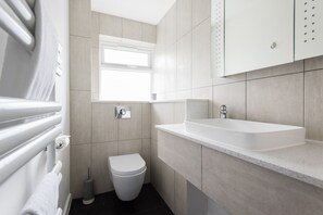 A modern bathroom with a white toilet, a sink, and a window. - Second Nest Waterloo (London)