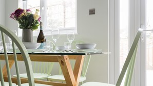 Una mesa de comedor con sillas, un jarrón con flores y una botella de vino.