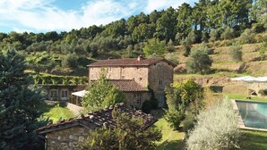 Une maison en pierre avec un toit de tuiles, entourée d’une végétation luxuriante et dotée d’une piscine.