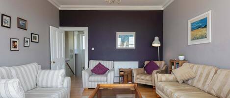 Een woonkamer met gestreepte banken, een houten salontafel en een kroonluchter.
