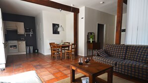 Ett vardagsrum med en soffa, ett soffbord och en matplats med ett bord och stolar. I bakgrunden syns ett kök.