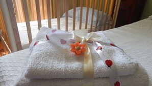 A neatly folded white towel with a ribbon and a flower, placed on a bed with a white textured cover. - House in Tuscany immersed in greenery  (Foiano della Chiana)