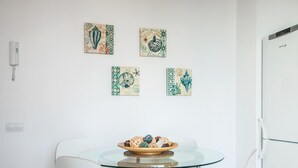 A dining area with a glass table and white chairs, a bowl of bread, and four decorative wall art pieces. - LOVELY POOL APARTMENT with PARKING 3 (Tossa de Mar)