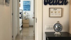 A hallway with a bed, a nightstand, a lamp, a framed picture, a wall clock, and a sign that reads "beach". - LOVELY POOL APARTMENT with PARKING 3 (Tossa de Mar)