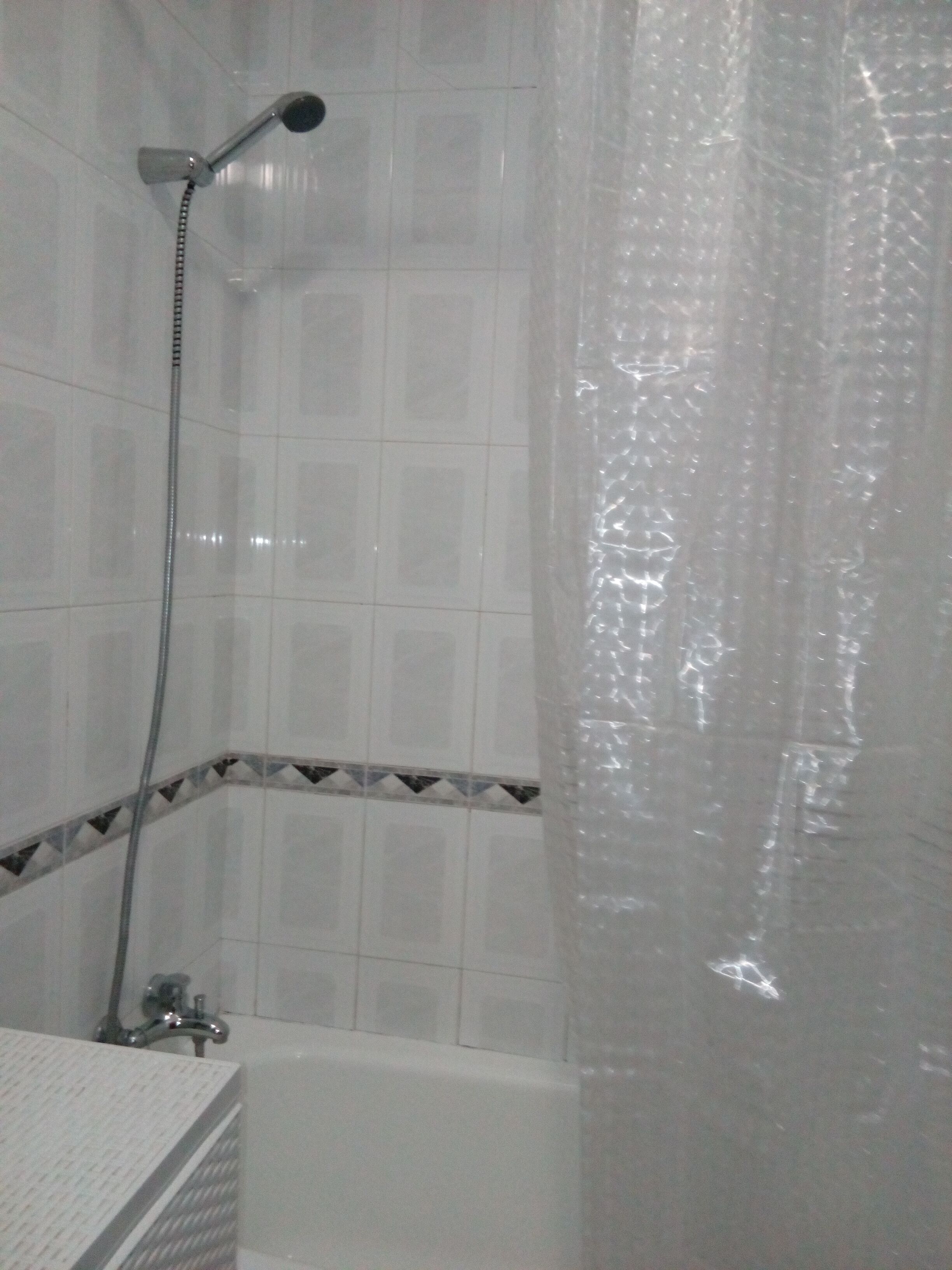 A bathroom with white tiled walls, a shower with a handheld showerhead, and a bathtub.