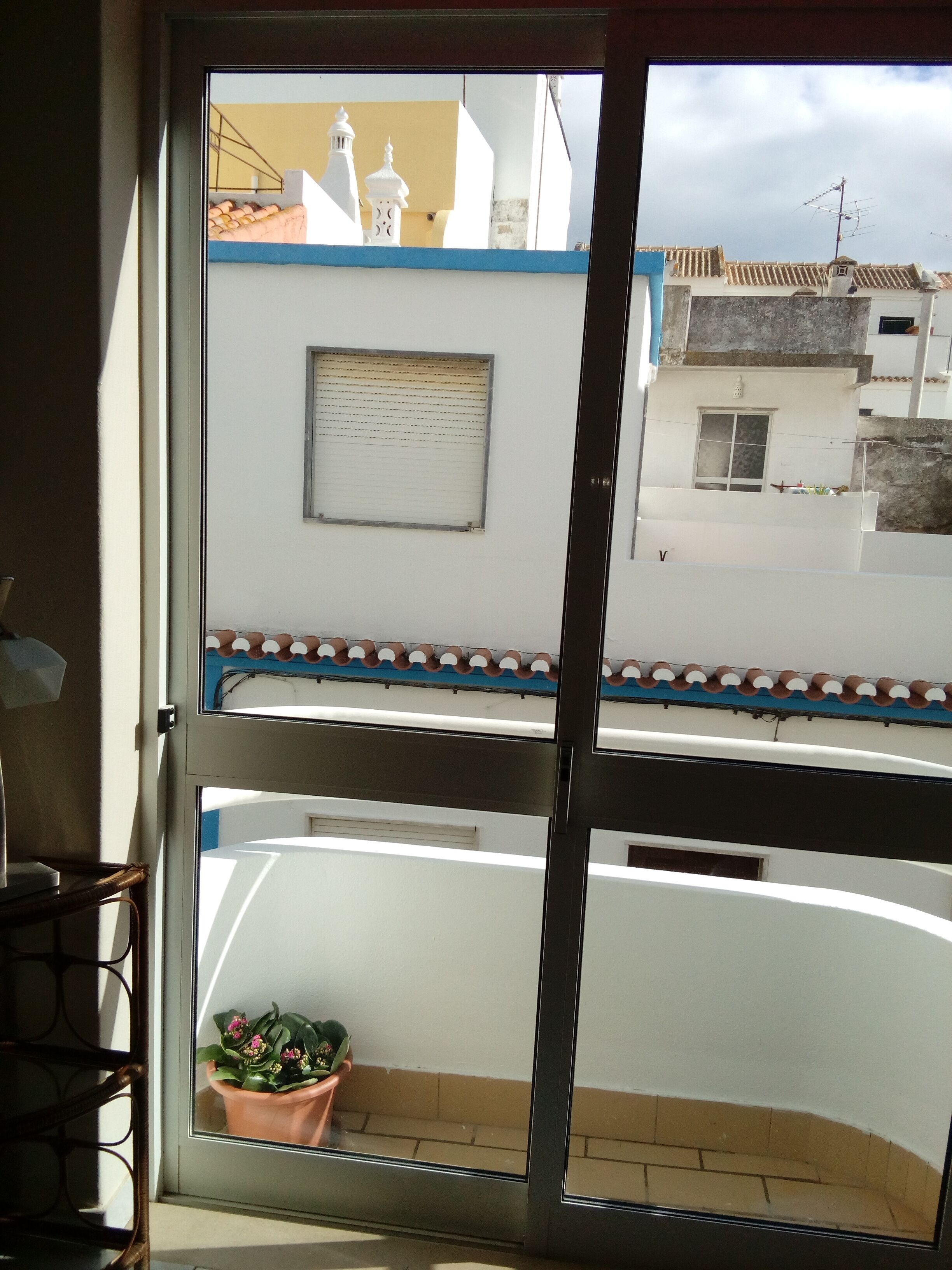 A balcony with a potted plant, a window with blinds, and a view of neighboring buildings.