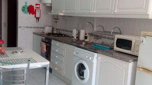 A compact kitchen with white cabinets, a washing machine, a microwave, and a dining area with a table and chairs. - 1 Bedroom Duplex with Balcony and Seaview (5-10 minutes form beach) (Alvor)