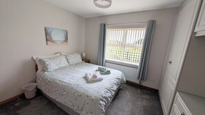 A bedroom with a bed, a window with curtains, a radiator, a small trash bin, and a painting on the wall. - Charming 3 Bedroom, Self Catering in centre of Mid Ulster close to Cookstown (Rock Dungannon)