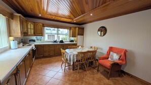 A kitchen with wooden cabinets, a dining table with chairs, a red chair, and a clock on the wall. - Charming 3 Bedroom, Self Catering in centre of Mid Ulster close to Cookstown (Rock Dungannon)