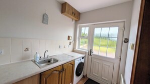 A compact kitchen with a sink, a washing machine, and a window with a view of greenery. - Charming 3 Bedroom, Self Catering in centre of Mid Ulster close to Cookstown (Rock Dungannon)