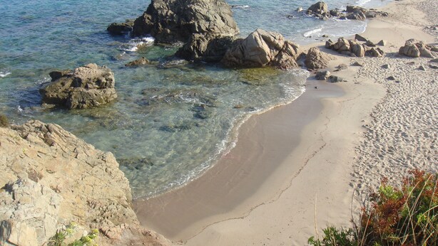 A beach with clear water, rocky formations, and sandy shores.