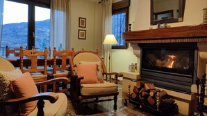 A cozy living room with a fireplace, wooden furniture, and a view of the outdoors. - OLIVILLAS GARDEN - BASE POINT ACCESS SIERRA NEVADA AND GRANADA (Güejar Sierra)