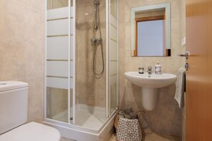 A bathroom with a glass-enclosed shower, a white sink, and a toilet.