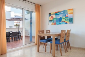 Un coin repas avec une table et des chaises, une porte vitrée donnant sur l’extérieur et un tableau abstrait aux couleurs vives accroché au mur.