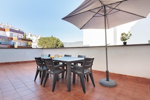 A terrace with a table and chairs, a large umbrella, and a potted plant.