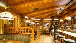 A restaurant with wooden interiors, hexagonal patterned flooring, and hanging lamps. - Panzl braü (Virgen)