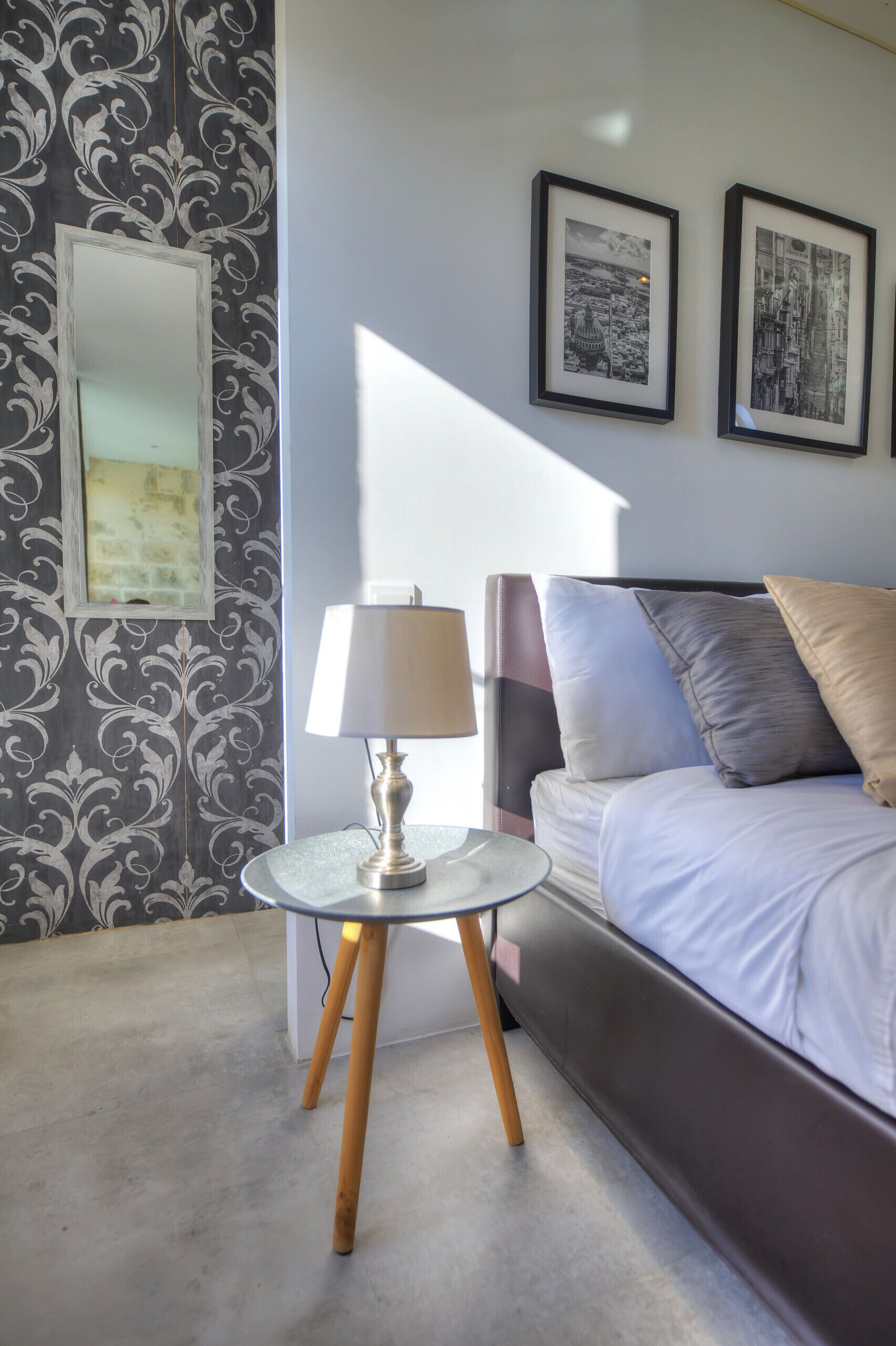 A bedroom with a bed, a bedside table with a lamp, and two framed pictures on the wall.