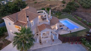 A two-story house with a swimming pool, outdoor seating, and a palm tree. - Hilltop Villa with Private Pool | Panoramic Views | Sea Turtle National Park.  (Zakynthos)