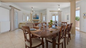 A dining area with a large wooden table, multiple chairs, and a chandelier. - Hilltop Villa with Private Pool | Panoramic Views | Sea Turtle National Park.  (Zakynthos)