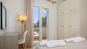 A hotel room with a bed, a desk, a chair, a lamp, and a sliding glass door leading to a balcony. - Hilltop Villa with Private Pool | Panoramic Views | Sea Turtle National Park.  (Zakynthos)