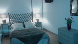 Quarto com cama, duas mesas de cabeceira com luminárias, cômoda e planta em vaso.