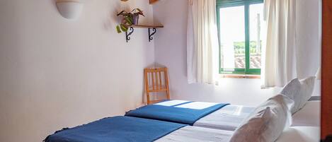Un dormitorio con dos camas, techo de madera, una ventana con cortinas y un estante pequeño con plantas.