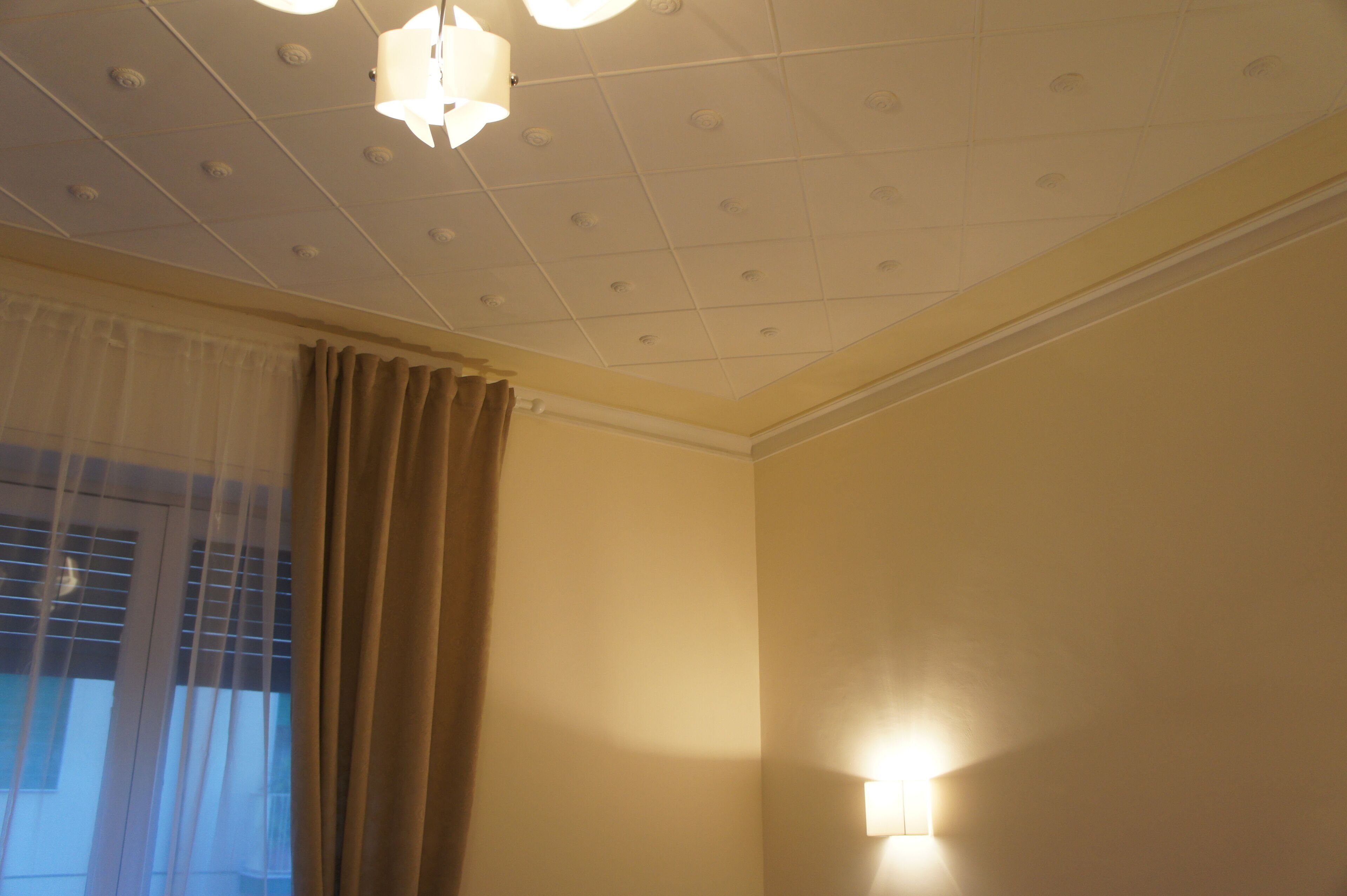 A room with a ceiling featuring recessed lighting and a wall-mounted light fixture.