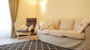 Un salon avec un canapé beige, un fauteuil à bascule en bois et un tapis à motifs.