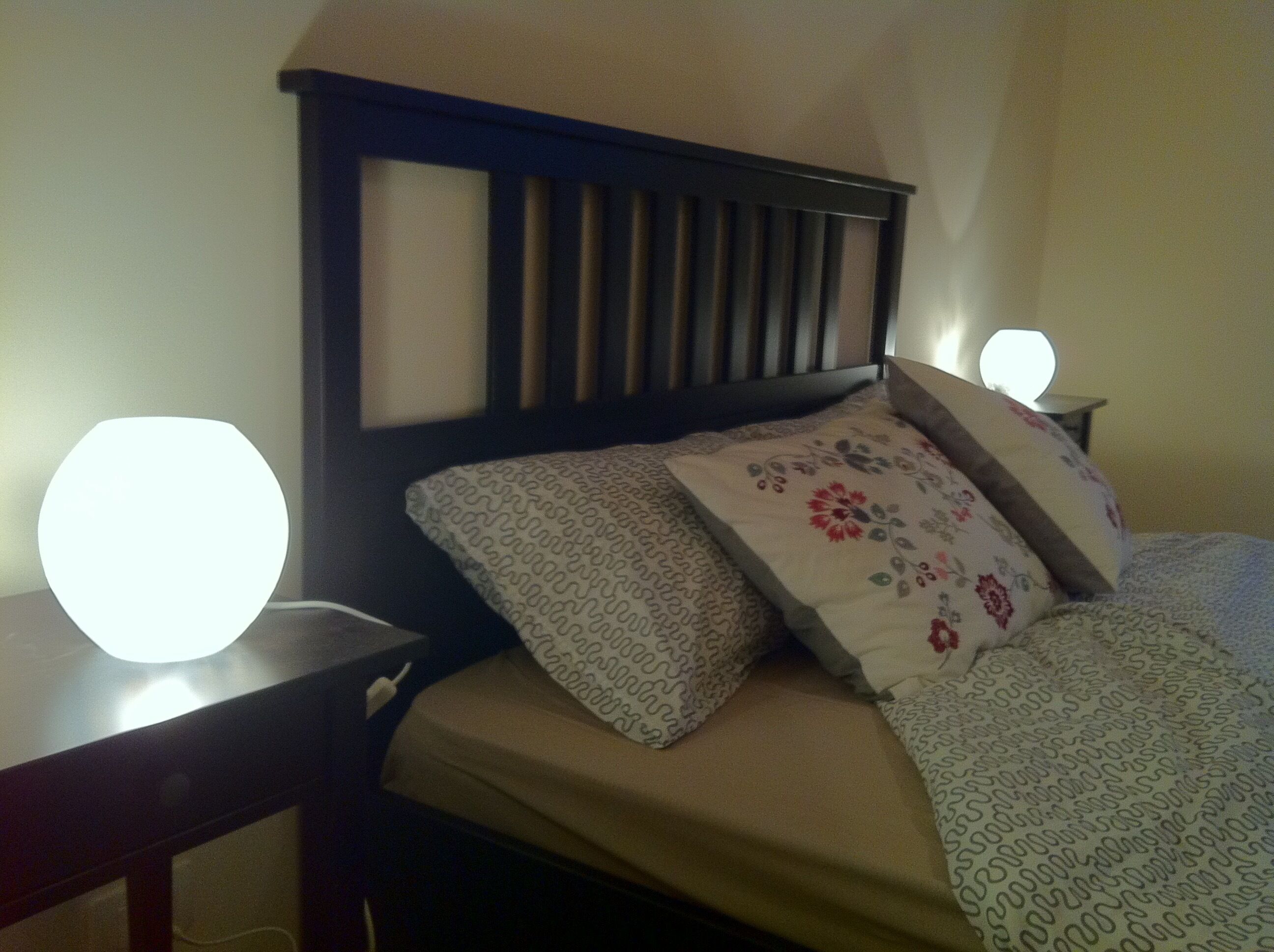 A bed with a wooden headboard, two bedside lamps, and patterned bedding.