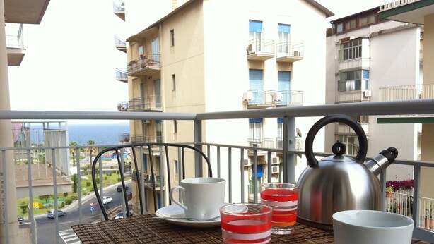 Un balcon avec une table préparée pour le thé, une bouilloire et des verres remplis d’une boisson rouge.
