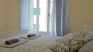 Une chambre à coucher avec une couvre-lit à motifs, une serviette enroulée posée sur une table de chevet et un oreiller orné d’un motif de feuilles.