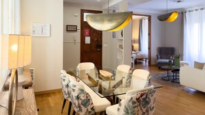 Ein modernes Wohnzimmer mit einem Glastisch, floralen Stühlen, einer Couch und einem großen Fenster mit Vorhängen.