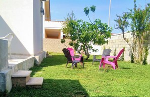 A grassy outdoor area with steps leading to a building, two chairs, and a tree.
