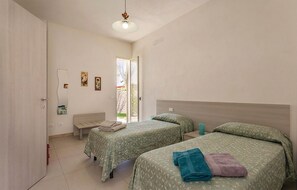 A bedroom with two beds, a bench, a door, and a window.
